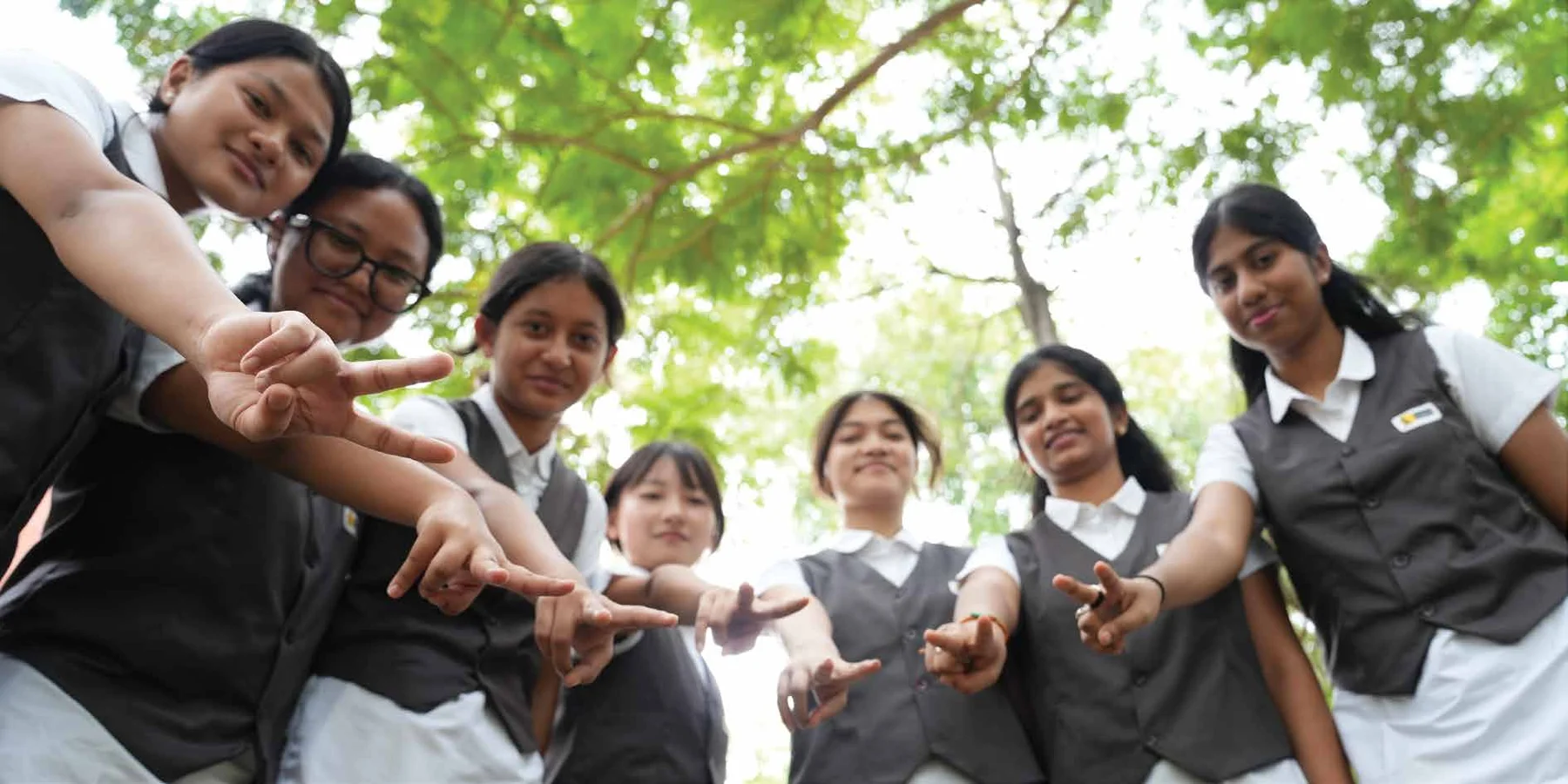 TVIS students reaching out together beneath the trees